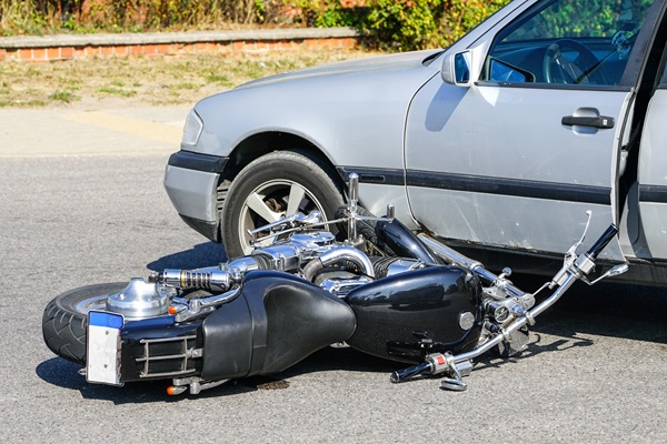 Black motorcycle lying on its side in front of a silver car with an open driver-side door, indicating a recent collision between the two vehicles.