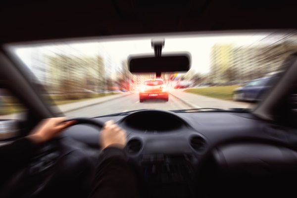 A blurred, first-person view from inside a car of a driver’s hands on the steering wheel as they approach another vehicle with glowing red brake lights on a street in Delaware.