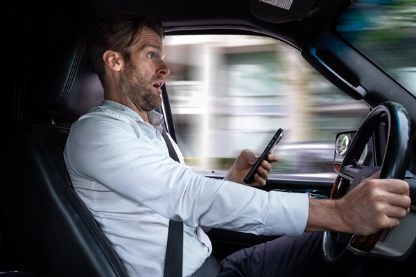 Driver looking startled while using a cellphone behind the wheel, illustrating how distracted driving can lead to sudden hazards and increase liability in car accident cases.